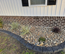 Finished decorative river rock bed with small green plants along a home foundation